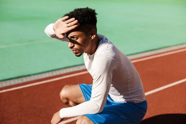 젊고 사려 깊은 아프리카 계 미국인 운동 선수는 시 경기장에서 태양으로 얼굴을 가리고 하나의 하치에 앉아 — 스톡 사진