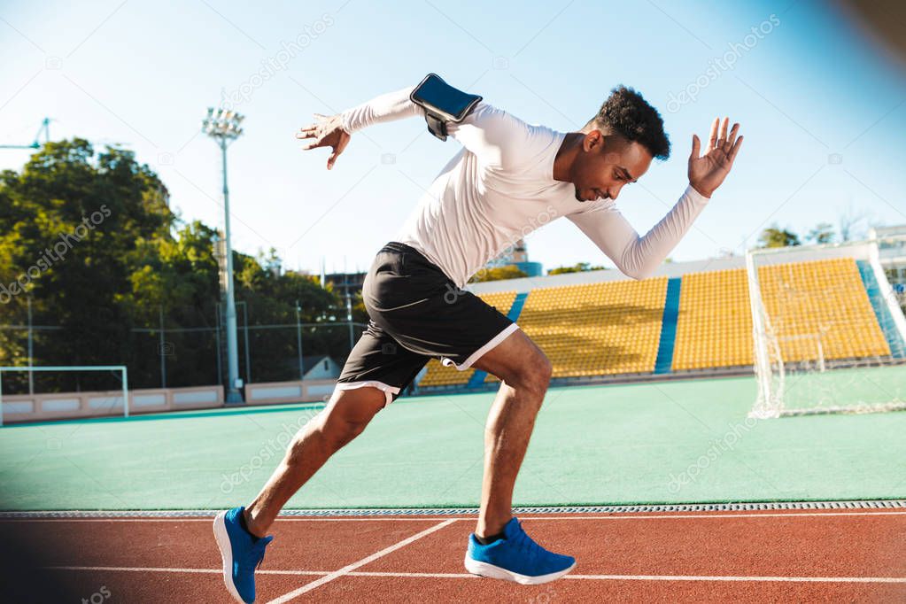 Side view of young African American sportsman running on racetrack during workout at city stadium