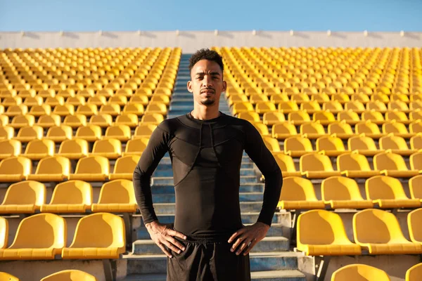 Młody przystojny Afroamerykanin sportowiec pewnie patrząc w aparacie wśród pusty stadion siedzenia — Zdjęcie stockowe