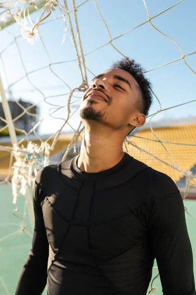 Portrét pohledného afroamerického sportovce zasněně stojící ve fotbalovém cíli na městském stadionu — Stock fotografie