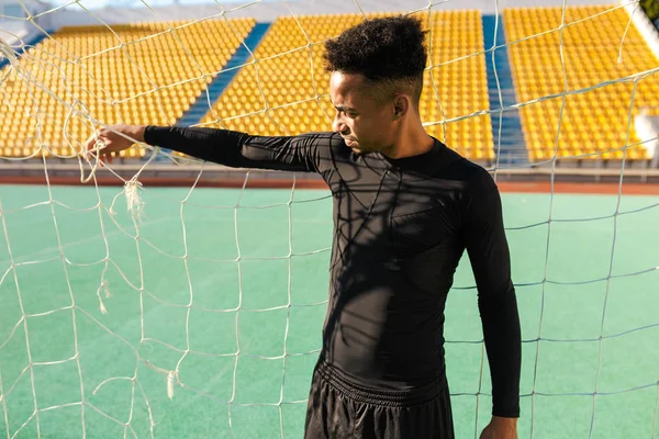 Mladý pohledný africký americký sportovec stojící ve fotbalovém cíli na městském stadionu — Stock fotografie