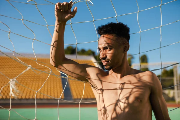 Retrato de atraente sem camisa esportista afro-americano pensativo olhando para longe no gol de futebol no estádio da cidade — Fotografia de Stock