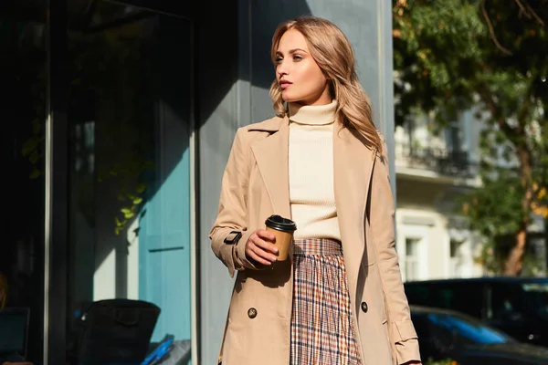 Menina loira elegante bonita em casaco bege com café para ir andando na rua da cidade — Fotografia de Stock