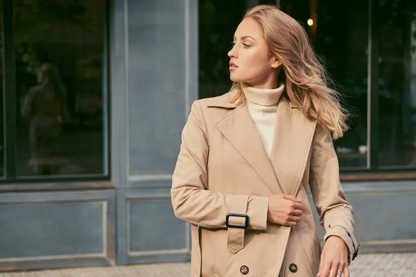 Vista lateral de la atractiva chica rubia en gabardina con confianza mirando hacia otro lado en la calle — Foto de Stock