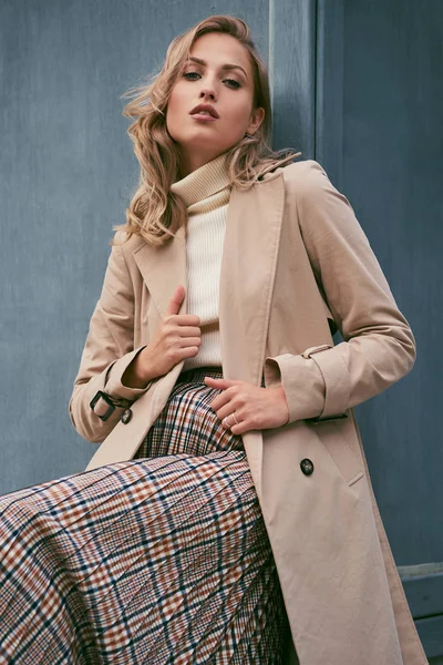 Beautiful casual blond girl in stylish trench coat confidently looking in camera outdoor — Stock Photo, Image