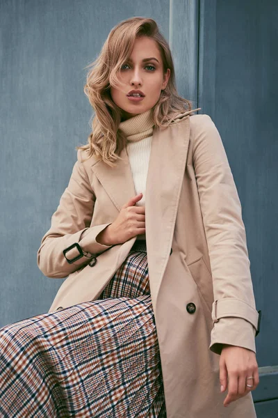 Beautiful serious casual blond girl in stylish trench coat sensually looking in camera outdoor — Stock Photo, Image