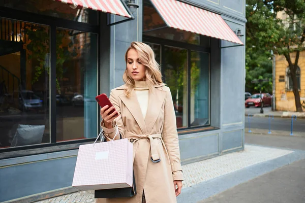 Schöne lässige blonde Mädchen in stilvollem Trenchcoat mit Shopping — Stockfoto
