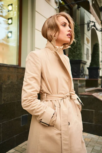 Vista lateral de la atractiva chica rubia con estilo en abrigo beige en la calle de la ciudad — Foto de Stock