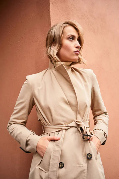 Side view of serious casual blond girl in beige trench coat confidently looking away outdoor — Stock Photo, Image