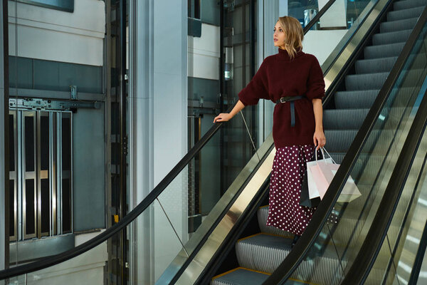 "Стильная" девушка с сумками для покупок на эскалаторе в современном торговом центре
