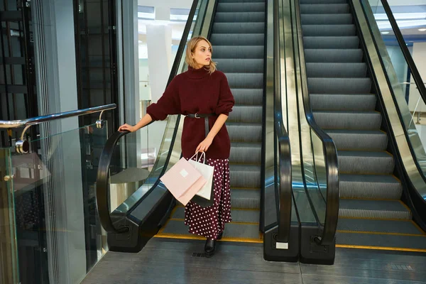 Hermosa chica rubia casual en escaleras mecánicas en el centro comercial moderno — Foto de Stock