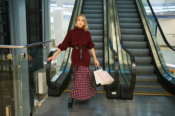 Atractiva chica rubia con estilo con bolsas de compras en la escalera mecánica en el centro comercial moderno — Foto de Stock