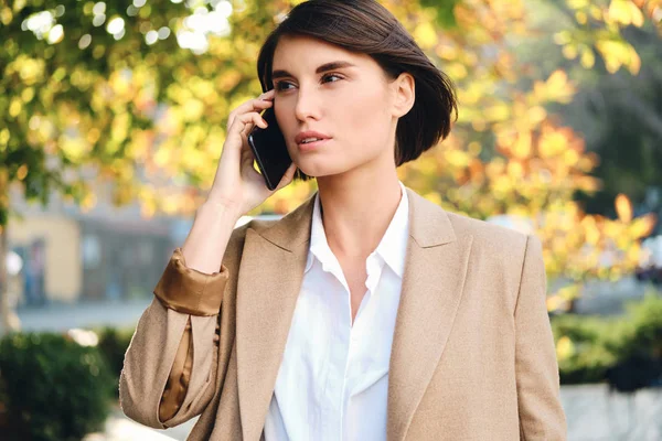 Молодая красивая стильная деловая женщина задумчиво разговаривает по мобильному телефону на открытом воздухе — стоковое фото