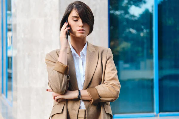 Giovane donna d'affari elegante e sicura di sé in giacca e cravatta parlare sul cellulare all'aperto — Foto Stock