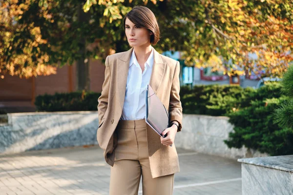 Молодая красивая стильная деловая женщина в костюме с папкой пристально глядя на улицу — стоковое фото