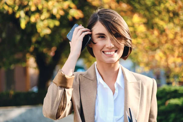 Portrait of pretty smiling business woman with cellphone happily looking away outdoor — Stok Foto