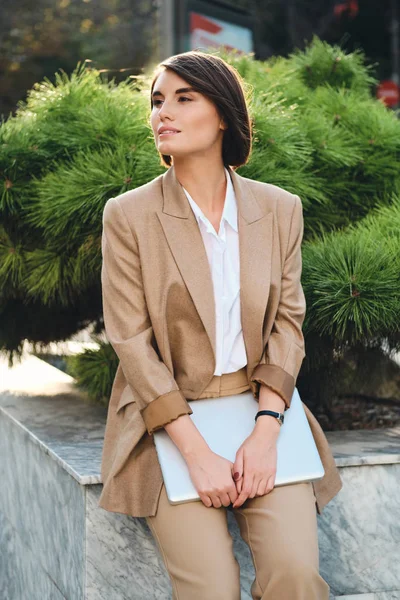 Jovem atraente mulher de negócios elegante em terno bege com laptop sonhadoramente lado ao ar livre — Fotografia de Stock