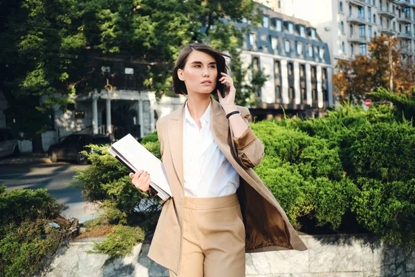 Junge attraktive Geschäftsfrau im beigen Anzug mit Laptop unterhält sich nachdenklich auf der Straße — Stockfoto