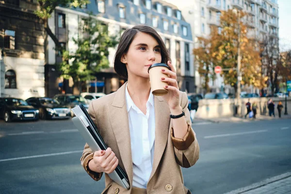 Nuori kaunis liikenainen kannettavan tietokoneen juominen kahvia tauon aikana kaupungin kadulla — kuvapankkivalokuva