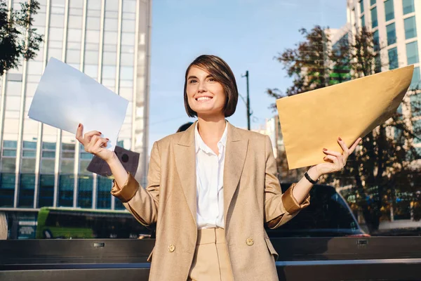 Молодая радостная деловая женщина держит конверт с ответом счастливо работает с бумагами на улице — стоковое фото