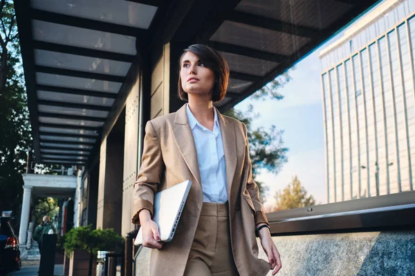 Молодая привлекательная стильная деловая женщина с ноутбуком задумчиво прогуливается по улице — стоковое фото