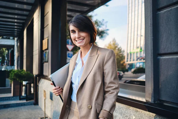 Giovane donna d'affari elegante allegra con computer portatile felicemente guardando in macchina fotografica su strada — Foto Stock