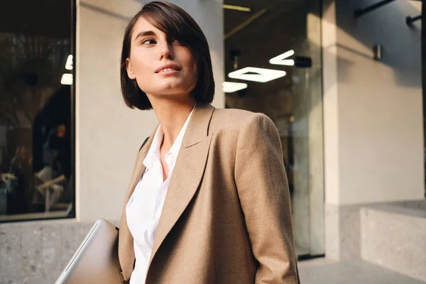 Retrato de jovem bela mulher de negócios elegante com laptop sonhadoramente olhando para longe na rua — Fotografia de Stock