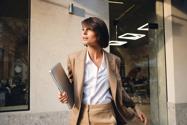 Vista laterale di giovane donna d'affari elegante con computer portatile pensieroso guardando lontano sulla strada della città — Foto Stock