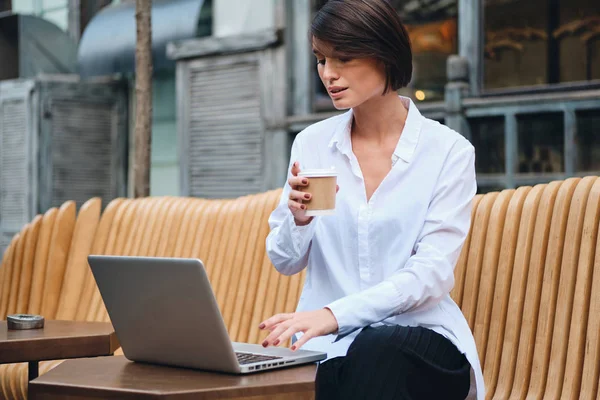 Νεαρή ελκυστική επιχειρηματίας που εργάζεται σε φορητό υπολογιστή κατά τη διάρκεια του διαλείμματος καφέ στο δρόμο — Φωτογραφία Αρχείου