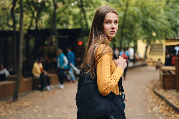 Krásná ležérní studentka s batohem soustředěně hledí do kamery v městském parku — Stock fotografie