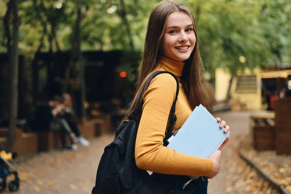 Całkiem uśmiechnięta studentka z książkami szczęśliwie patrząca w kamerę w parku miejskim — Zdjęcie stockowe