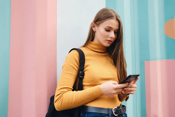 Houkutteleva rento opiskelija tyttö käyttää matkapuhelinta yli värikäs tausta ulkona — kuvapankkivalokuva