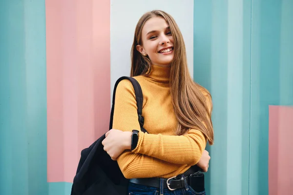 Красивая улыбающаяся случайная студентка радостно смотрит в камеру на красочном фоне под открытым небом — стоковое фото