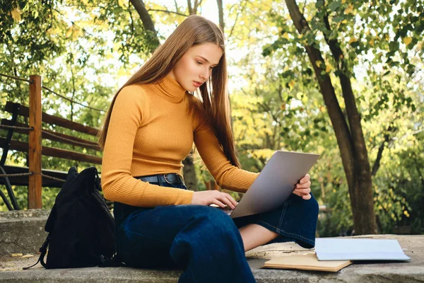 Houkutteleva rento opiskelija tyttö harkitsee opiskelee kannettavan kaupungin puistossa — kuvapankkivalokuva