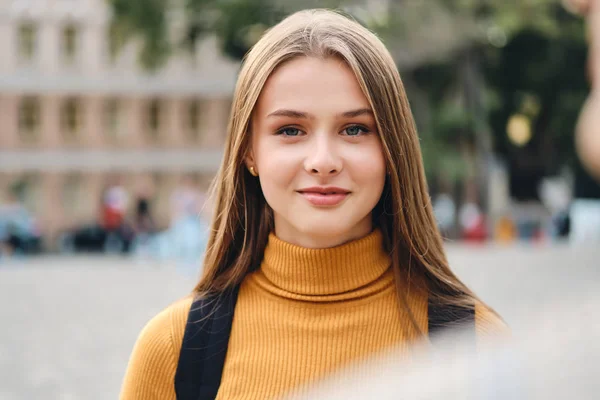 Portrét krásné usměvavé ležérní studentka zasněně dívá do kamery na ulici města — Stock fotografie