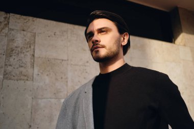 Genç, çekici, şık, esmer, omuzlarında paltosu olan bir adam düşünceli bir şekilde dışarı bakıyor.