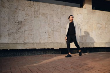 Palto giymiş yakışıklı genç bir adam düşünceli bir şekilde dışarı bakıyor.