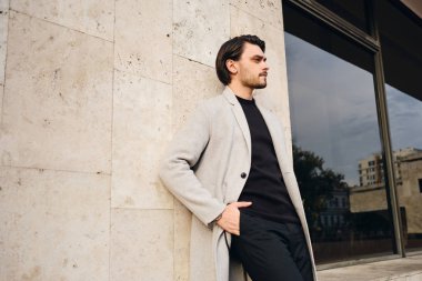 Ceketli, elleri ceplerinde şık bir adamın yan görünüşü.