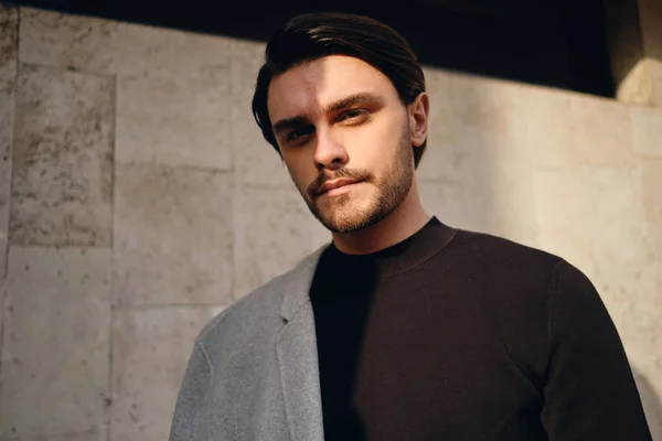 Retrato de jovem atraente homem elegante com casaco no ombro olhando com confiança na câmera ao ar livre — Fotografia de Stock
