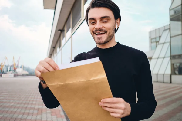 Jovem morena alegre homem feliz abertura envelope com resposta de trabalho ao ar livre — Fotografia de Stock