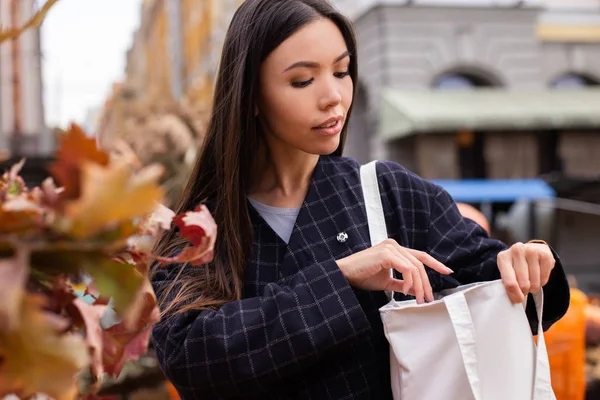 Porträt einer jungen schönen, lässigen Frau, die im herbstlichen Hofladen im Freien nachdenklich nach Geldbörse in der Tasche sucht — Stockfoto