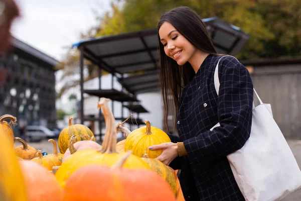 Młoda atrakcyjna kobieta casual szczęśliwie kupuje dynię na dzień Halloween w jesiennym sklepie gospodarstwa na świeżym powietrzu — Zdjęcie stockowe