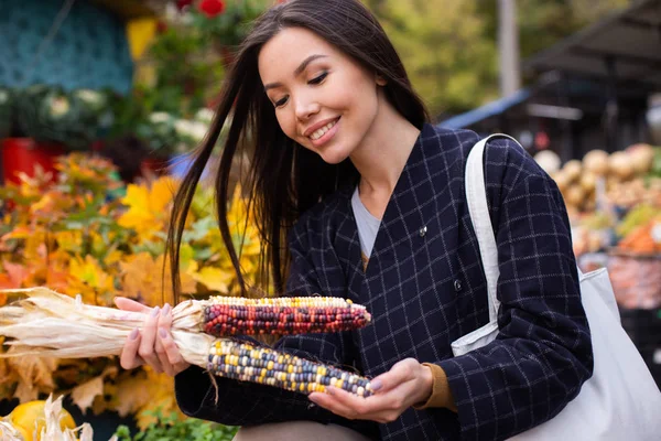 Молодая привлекательная случайная женщина с радостью покупает красочную кукурузу на открытом воздухе в магазине осенней фермы — стоковое фото