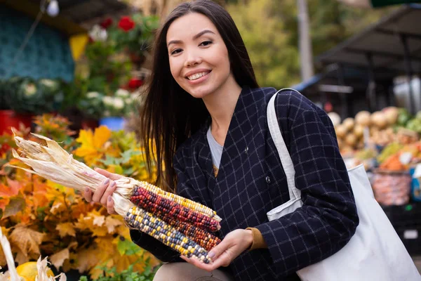 Jonge vrolijke vrouw gelukkig op zoek in de camera kopen kleurrijke maïs in de herfst boerderij winkel buiten — Stockfoto