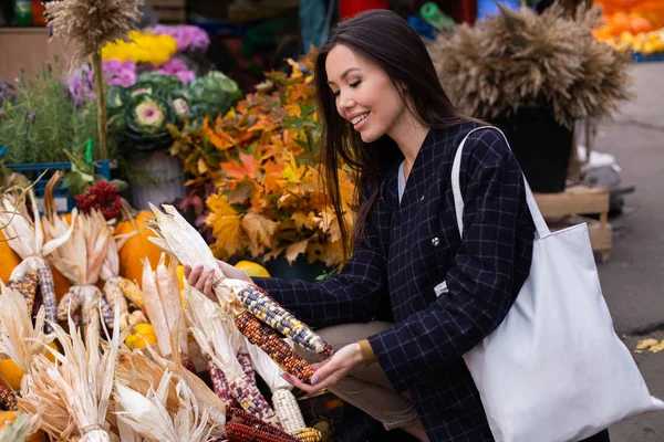 Ung, vakker kvinne kjøper gladelig fargerik mais til Halloween-dagen utendørs på høstfarmen. – stockfoto