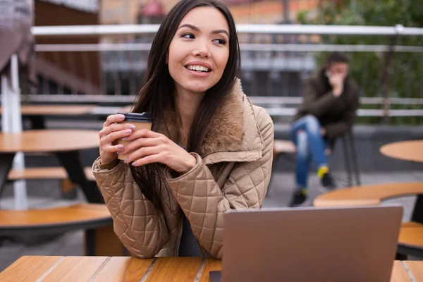 Jong mooi glimlachen casual vrouw in donsjas met laptop gelukkig drinken koffie in cafe op straat — Stockfoto
