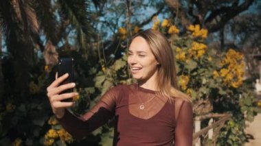 Akıllı telefonu kullanan güzel bir kız şehir parkında yürürken ailesiyle görüntülü konuşma yapıyor. Çekici genç bir kadın görüntülü konuşma yapıyor.