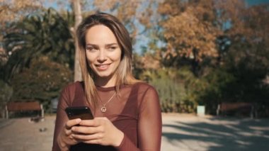 Güzel sarışın flörtçü kız akıllı telefon kullanıyor rüyasında parkta erkek arkadaşıyla mesajlaşıyor. Çekici utangaç kız dudaklarını ısıran mesaj atıyor.