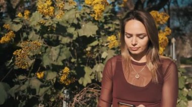 Parkta yürürken erkek arkadaşıyla akıllı telefon mesajlaşması yapan oldukça üzgün bir kız. Akıllı telefonu düşünceli bir şekilde kullanan çekici kız.