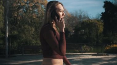 Kırmızı elbiseli genç bir kadının gölün kenarındaki parkta yürürken görüntüsü. Telefondaki çekici sarışın kızın görüntüsü.